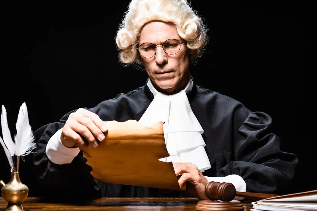 stock-photo-judge-judicial-robe-wig-sitting-table-reading-document-isolated-black.jpg